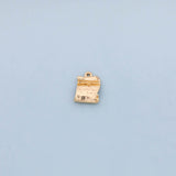 May include: A small, gold-colored charm in the shape of a rolled-up scroll. The charm has a textured surface and a small loop at the top for attaching to a necklace or bracelet. The scroll appears to have some faint markings.