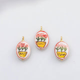 May include: Three oval-shaped pendants with a hand-painted floral design. Each pendant features a white background with a red border, a yellow pot, and pink flowers. The pendants have gold-colored loops at the top.