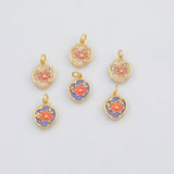 May include: Six gold-colored pendants with a floral design. Each pendant features a red flower with white and purple accents. The pendants have a small loop at the top for attaching to a chain or bracelet. Small clear crystals are set around the flower.