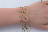 May include: Gold-colored chain bracelets with colorful enamel accents in green, pink, blue, and other shades. The bracelets are displayed on a person's wrist, showcasing the jewelry's design and color variations.