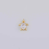 May include: A gold-colored turtle pendant with a clear, oval-shaped gemstone at its center. The pendant has a small loop at the top for attaching to a chain or bracelet. The turtle's flippers and head are also gold-colored.