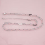 May include: Silver-toned chain necklace with elongated oval links. The necklace has a lobster clasp closure and an adjustable chain. The links are connected in a paperclip style. The background is a soft pink.