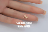 May include: A small, gold-colored charm in the shape of a checkered racing flag. The charm is held on a finger. The text "14K Gold Filled Made in USA" is displayed below the charm.