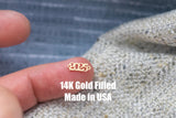May include: Close-up of a gold-filled charm with the year 2025 engraved on it. The charm is being held by a finger. The text "14K Gold Filled Made in USA" is visible below the charm.
