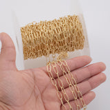 May include: A spool of gold-colored chain with oval links. The chain is displayed in a hand, with a portion of the chain extending from the spool. The chain is a bright, shiny gold color.