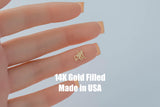 May include: A small, gold-colored charm in the shape of a person playing hockey. The charm is held between fingers. The text "14K Gold Filled Made in USA" is displayed in white block letters.