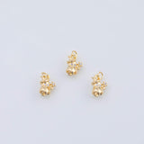 May include: Three gold-colored charms in the shape of a bell with a small flower and a clear gem. The charms are on a white background. The charms have a loop at the top for hanging.